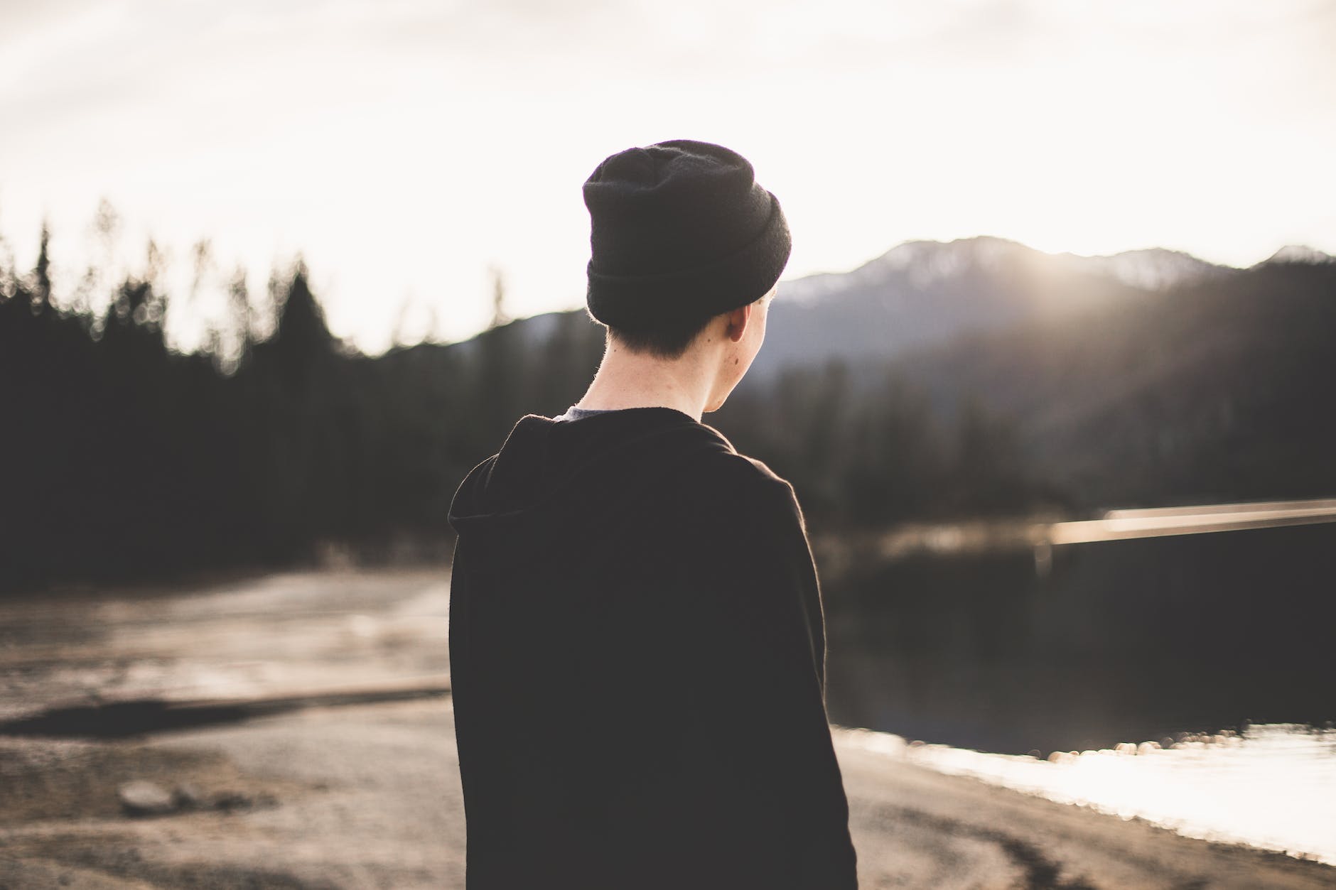 selective focus photography of man standing on brown soil facing body of water